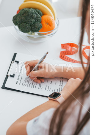 Woman writing information into the notepad. Professional medical worker in white coat is in the office Woman writing information into the notepad. Professional medical worker in white coat is in the office 124040474