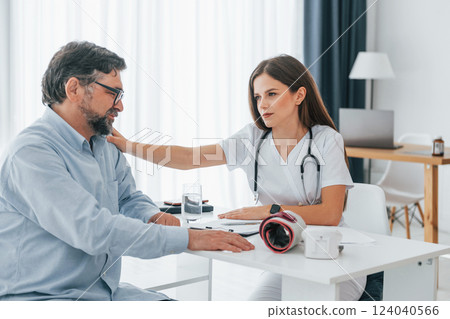 Mature man is with female doctor, having consultation. Professional medical worker in white coat is in the office Mature man is with female doctor, having consultation. Professional medical worker in white coat is in the office 124040566