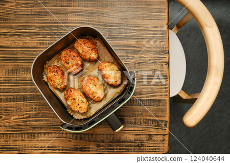 Roasted meat patties in an air fryer basket, resting on a wooden table 124040644