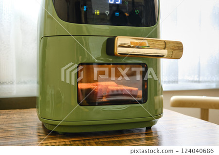 Modern green air fryer cooking food on a wooden table in bright kitchen setting Modern green air fryer cooking food on a wooden table in bright kitchen setting 124040686