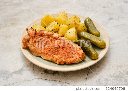 Delicious pork chop served with tender potatoes and pickles on a simple plate Delicious pork chop served with tender potatoes and pickles on a simple plate 124040706