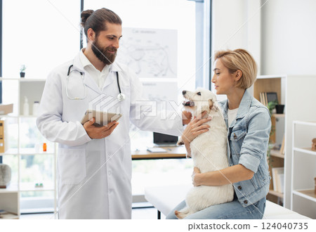 Male veterinarian discussing pet health with woman owner holding dog during examination in clinic. Male veterinarian discussing pet health with woman owner holding dog during examination in clinic. 124040735