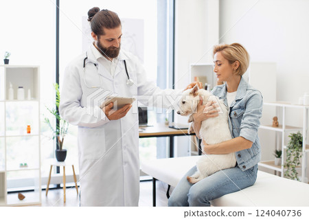 Man veterinarian in white coat and woman pet owner with dog during medical checkup, showing professional and caring environment in modern animal clinic 124040736