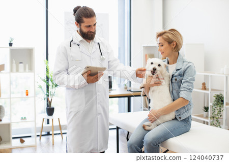Man veterinarian in white coat and woman pet owner with dog during medical checkup, showing professional and caring environment in modern animal clinic Man veterinarian in white coat and woman pet owner with dog during medical checkup, showing professional and caring environment in modern animal clinic 124040737