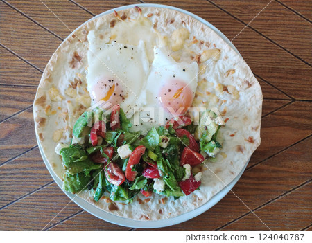Delicious breakfast with fried eggs, fresh salad, and flatbread served on a wooden plate 124040787