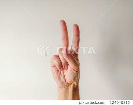 Closeup of a hand displaying the peace sign against a neutral background. Perfect for concepts of peace, unity, victory, or number two. Versatile image for websites, presentations, and social media. Closeup of a hand displaying the peace sign against a neutral background. Perfect for concepts of peace, unity, victory, or number two. Versatile image for websites, presentations, and social media. 124040815