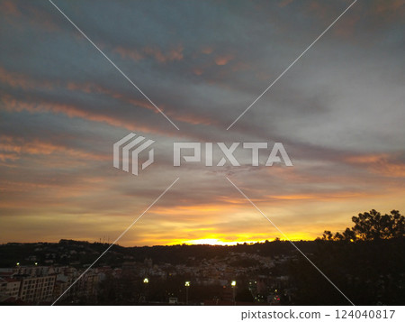 Stunning sunset over a cityscape. Warm golden hues paint the sky, contrasting beautifully with the dark silhouettes of buildings and trees. Ideal for travel, nature, or citythemed projects. 124040817