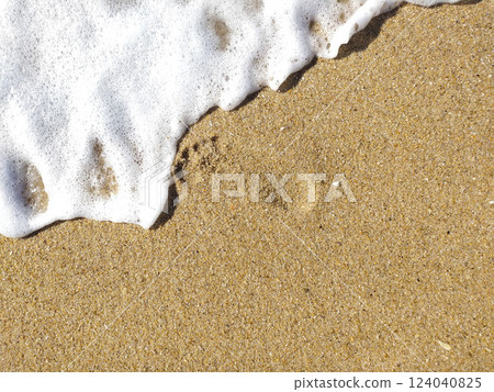 Gentle waves rolling onto sandy beach at sunrise, creating bubbles and a shimmering surface 124040825