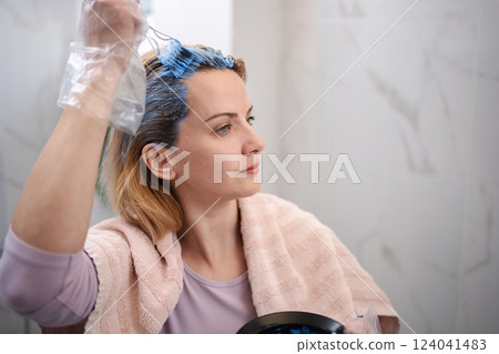 Woman dyeing her hair at home with a towel around her shoulders 124041483