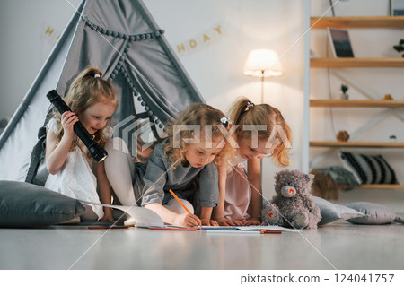 Girl holding flashlight. Other one draw on the ground with paper. Group of children is together at home at daytime 124041757