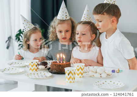 Sitting by the table with cake. Celebrating birthday. Group of children is together at home at daytime 124041761