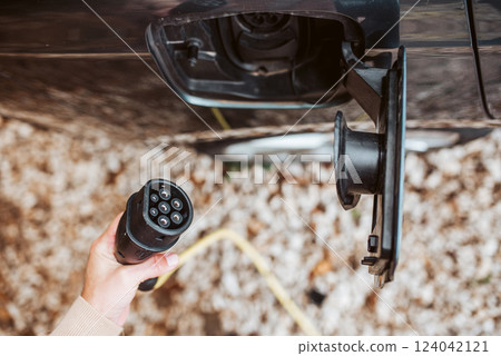 Man charging electric car, hodding charger in hand. 124042121