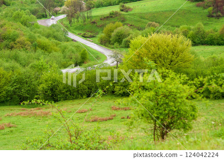 travel landscape, with road through valley. green nature scenery in spring for tourism. beautiful rural background view from the hill with forest. outdoor adventure in the rain 124042224