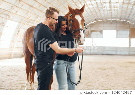 Man with his pregnant wife that is in casual clothes is standing with the horse on a stable 124042497
