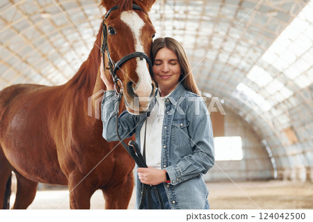 Smiling and enjoying. Young woman in jeans clothes is with horse on a stable Smiling and enjoying. Young woman in jeans clothes is with horse on a stable 124042500