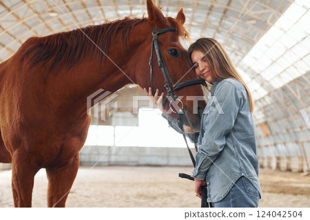 Young woman in jeans clothes is with horse on a stable 124042504