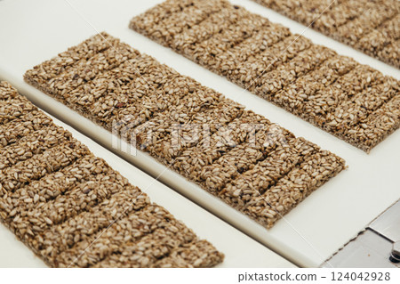 Gozinaki made from sunflower seeds with sugar syrup transferring by conveyor at sweet industry Gozinaki made from sunflower seeds with sugar syrup transferring by conveyor at sweet industry 124042928