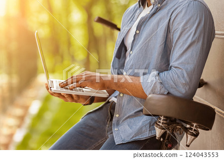 Unrecognizable black man leaning on bicycle and using laptop outdoors, side view, cropped image with free space 124043553