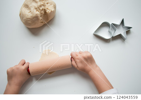 Child rolling dough with cookie cutters on white surface Child rolling dough with cookie cutters on white surface 124043559