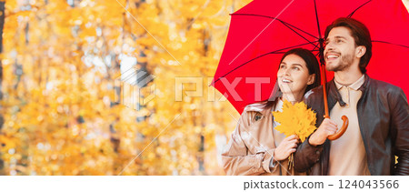 Happy lovers walking under red umbrella at rainy autumn day by forest, panorama with free space Happy lovers walking under red umbrella at rainy autumn day by forest, panorama with free space 124043566