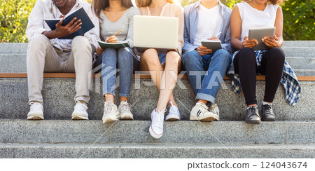 Cropped of international students doing homework on stairs in city, using laptop, taking notes, education concept Cropped of international students doing homework on stairs in city, using laptop, taking notes, education concept 124043674