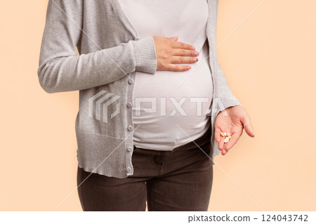 Medicines During Pregnancy. Unrecognizable Pregnant Woman Showing Pills In Hand Touching Belly Standing On White Background In Studio. Cropped Medicines During Pregnancy. Unrecognizable Pregnant Woman Showing Pills In Hand Touching Belly Standing On White Background In Studio. Cropped 124043742