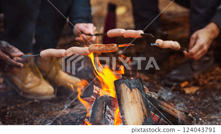 Cropped of mixed race group of friends sitting beside fireplace and frying sausages in forest Cropped of mixed race group of friends sitting beside fireplace and frying sausages in forest 124043791
