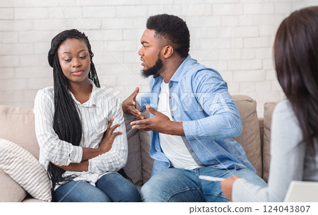 Anxious black man blaming his indifferent wife during therapy counselling session, emotionally gesturing while sitting on couch in counselor's office. Anxious black man blaming his indifferent wife during therapy counselling session, emotionally gesturing while sitting on couch in counselor's office. 124043807