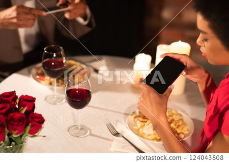 Modern Relationship. Millennial Afro Couple Taking Photo Of Food On Phones During Romantic Dinner In Fancy Restaurant. Cropped, Selective Focus Modern Relationship. Millennial Afro Couple Taking Photo Of Food On Phones During Romantic Dinner In Fancy Restaurant. Cropped, Selective Focus 124043808