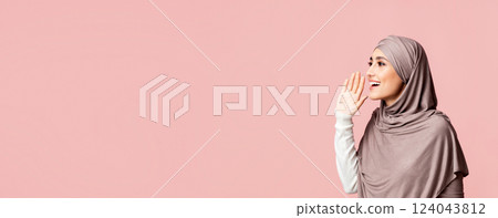 Beautiful muslim girl in hijab shouting at copy space, making announcement, sharing news on pink studio background. 124043812