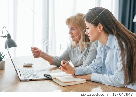Sitting by table with laptop. Mother and daughter is together at home Sitting by table with laptop. Mother and daughter is together at home 124043948