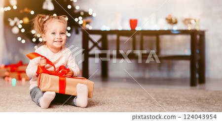 Christmas Eve. Curious little girl opening xmas gift at home, free space 124043954