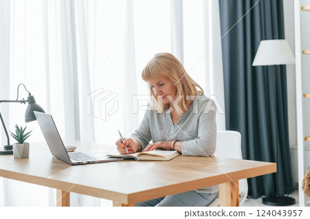 Sitting by table with laptop. Senior woman with red hair is at home alone 124043957