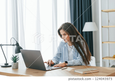 Freelance worker is sitting by table with laptop. Young beautiful woman is home alone in domestic room 124043973