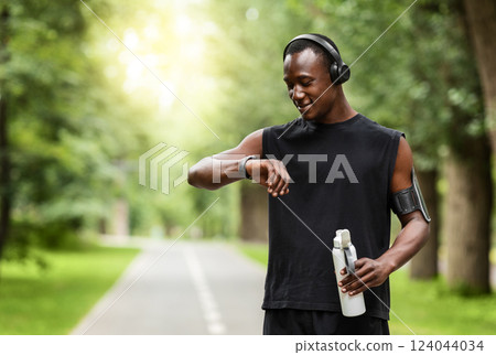 Modern technologies and active lifestyle. African sportsman working out with fitness bracelet, drinking water, blurred park background, copy space Modern technologies and active lifestyle. African sportsman working out with fitness bracelet, drinking water, blurred park background, copy space 124044034