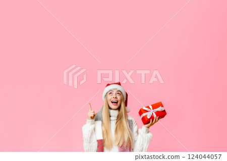 Time to buy christmas gifts. Excited girl in santa hat with gift box pointing at copy space 124044057