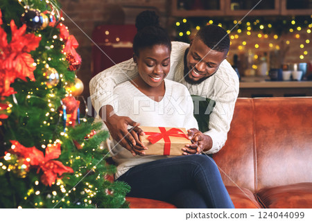Happy african american girl received Christmas present from her caring boyfriend, looking at gift box with excitement. Happy african american girl received Christmas present from her caring boyfriend, looking at gift box with excitement. 124044099