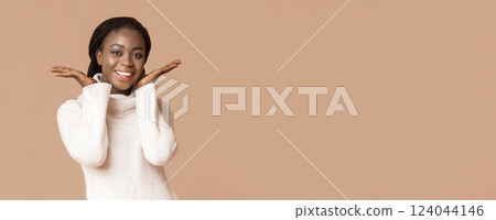 Portrait of sweet african woman touching her cheeks with hands over beige background, panorama with copy space 124044146