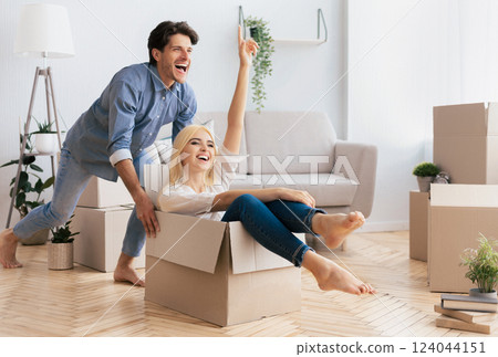 Home Owners. Couple Having Fun In New House. Man Riding Woman In Moving Box Celebrating Buying Own Apartment. Copy Space Home Owners. Couple Having Fun In New House. Man Riding Woman In Moving Box Celebrating Buying Own Apartment. Copy Space 124044151