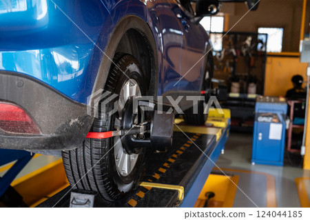 Wheel alignment equipment grip the tire of car wheel in car repair shop. Auto wheel alignment in workshop of service station. Car wheel balance. Suspension adjustment. Vehicle inside garage workshop. Wheel alignment equipment grip the tire of car wheel in car repair shop. Auto wheel alignment in workshop of service station. Car wheel balance. Suspension adjustment. Vehicle inside garage workshop. 124044185