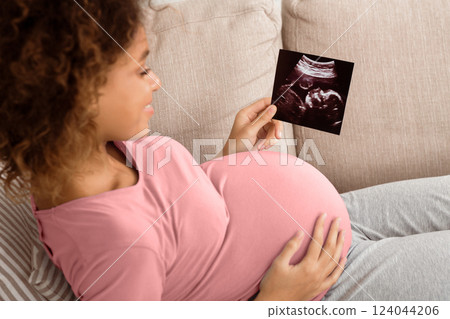 African-american pregnant woman holding ultrasound scan, relaxing on couch African-american pregnant woman holding ultrasound scan, relaxing on couch 124044206
