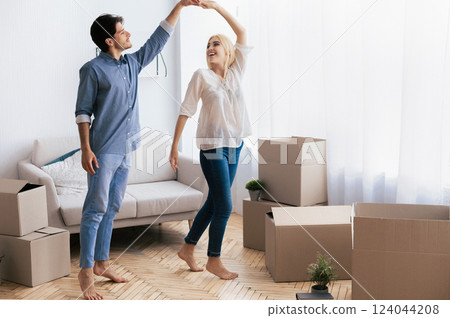 Happy Relocation. Man And Woman Dancing Among Moving Boxes In New Flat Apartment Or House. Free Space For Text Happy Relocation. Man And Woman Dancing Among Moving Boxes In New Flat Apartment Or House. Free Space For Text 124044208