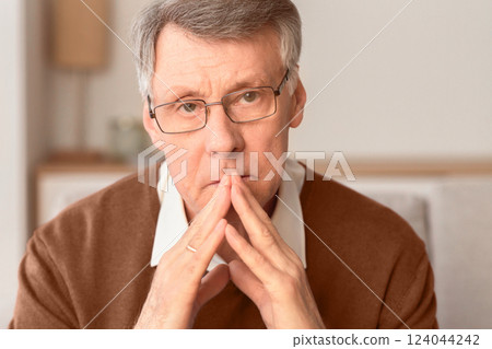 Portrait Of Serious Senior Man Thinking About Retired Life Holding Hands Near Face Sitting On Sofa Indoor. Selective Focus Portrait Of Serious Senior Man Thinking About Retired Life Holding Hands Near Face Sitting On Sofa Indoor. Selective Focus 124044242
