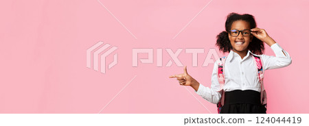 African American Schoolgirl Pointing Finger Aside At Free Space Recommending Something Over Yellow Studio Background. Panorama 124044419