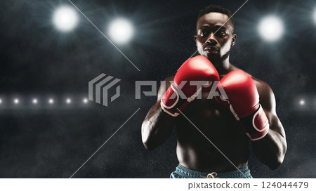 A boxer stands ready in a boxing ring, wearing red gloves and looking determined. 124044479