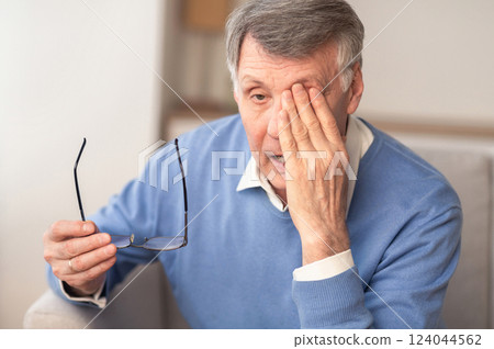 Glaucoma. Tired Elderly Man Massaging Eye Holding Eyeglasses Having Eyestrain And Ocular Tension Sitting On Couch At Home. Selective Focus 124044562