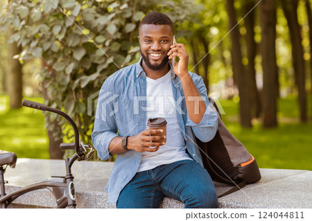 African American Man Employee Drinking Coffee In Park And Talking On Cellphone, Relaxing Outdoors During Break At Work 124044811