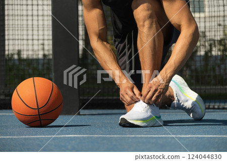 Close up basketball player tying sports shoes in basketball court outdoors. Last preparation. Summer game. 124044830