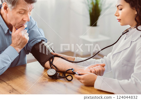 Cardiology. Mexican nurse measuring blood pressure of elderly man with hypertensive crisis at clinic office, copyspace 124044832