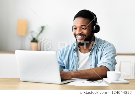 Cheerful black freelancer working on laptop and listening music in headphones, copy space 124044833